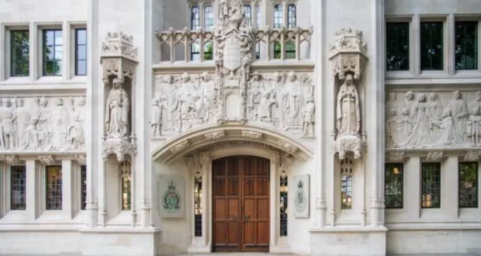 Ornate stone facade of a courthouse building featuring statues and intricate carvings above a large wooden entrance door.