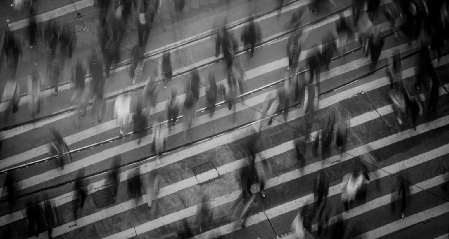 Motion-blurred image of pedestrians crossing a busy street, emphasizing urban movement and activity.