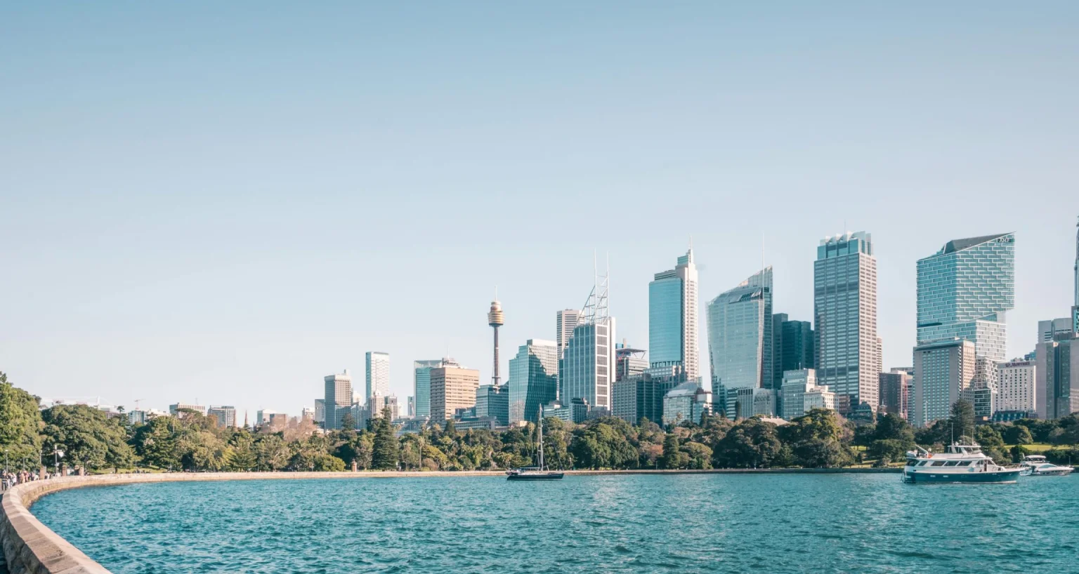 Scenic view of Sydney Harbour with the Opera House and city skyline in the distance, framed by calm blue water.