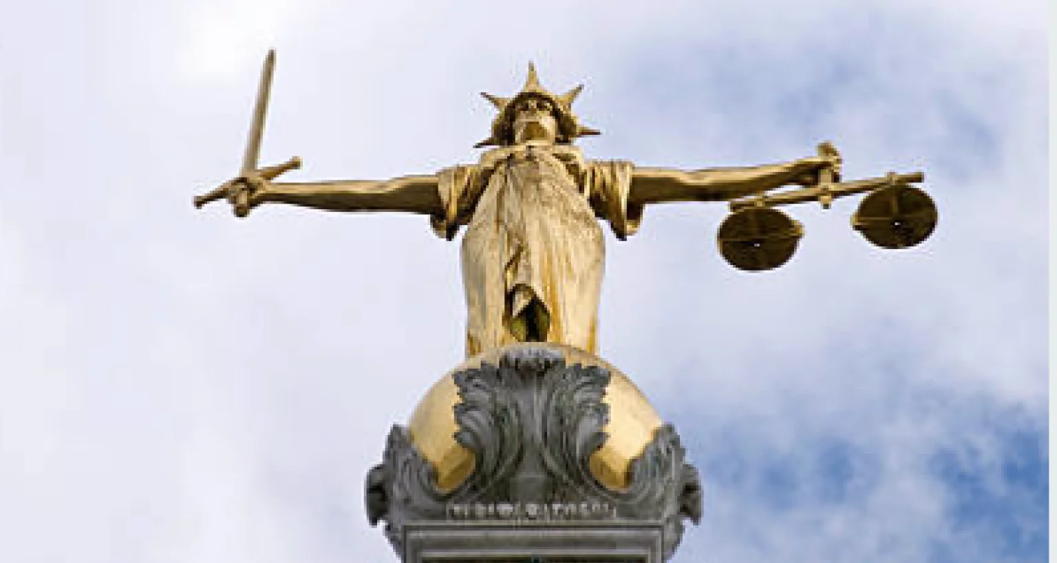 Statue of Lady Justice with scales and sword against a cloudy sky.