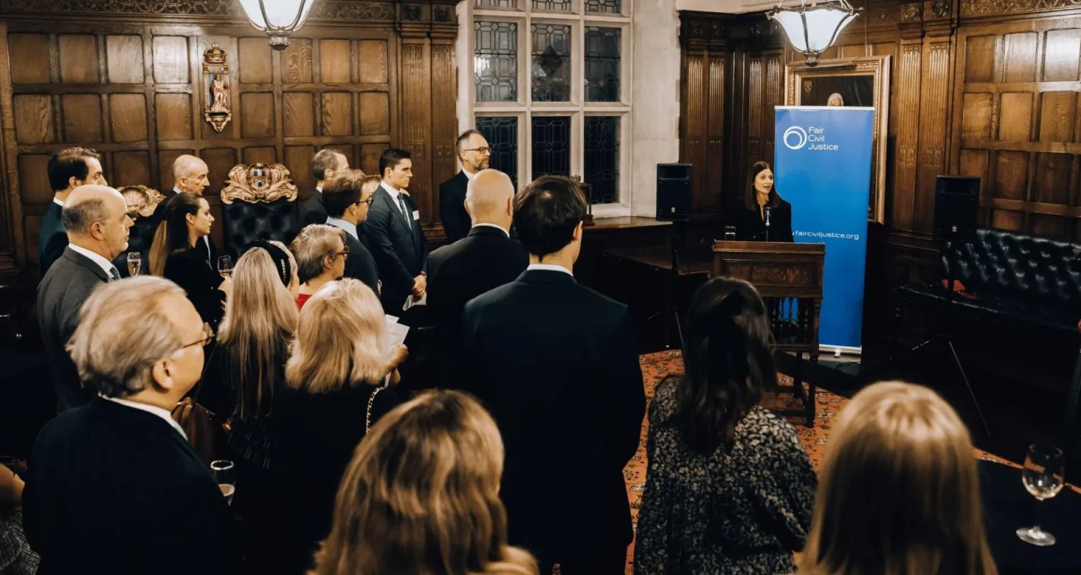 Conference audience in a wood-paneled room listening to a speaker presenting in front of a Fair Civil Justice banner.
