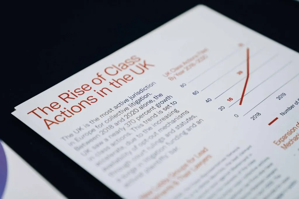 Close-up of a printed brochure titled 'The Rise of Class Actions in the UK,' detailing collective litigation trends with a graph showing growth from 2018 to 2020.